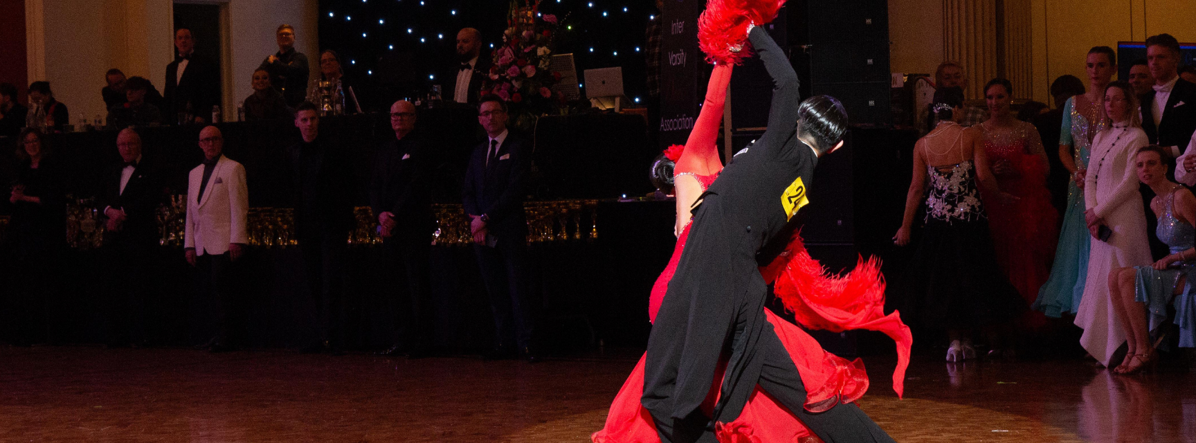 A man in a tuxedo dancing with a women in a red dress in a dancing competition
