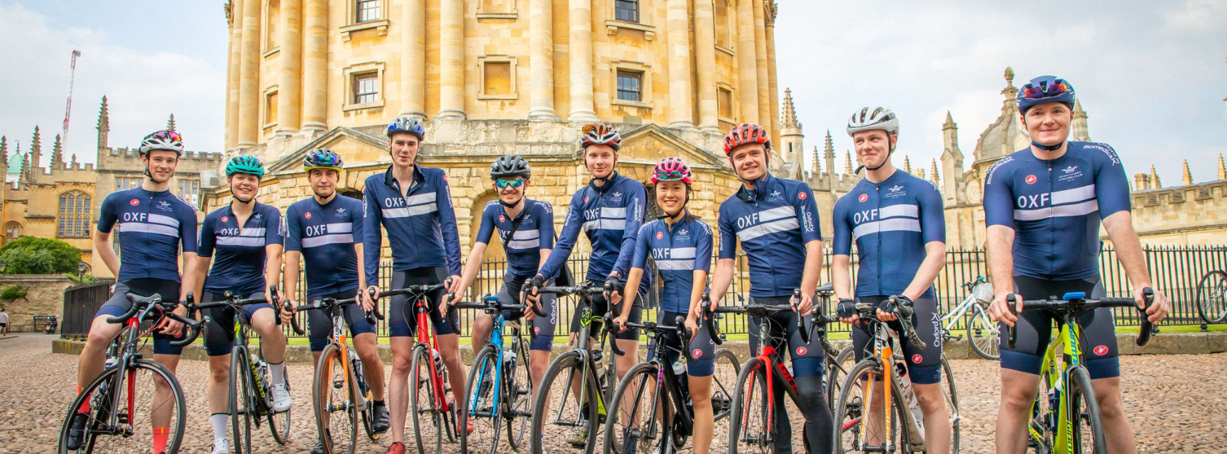 An image of cyclists in Oxford blue kit, posing with their bikes in front of the Radcliffe Camera in Oxford