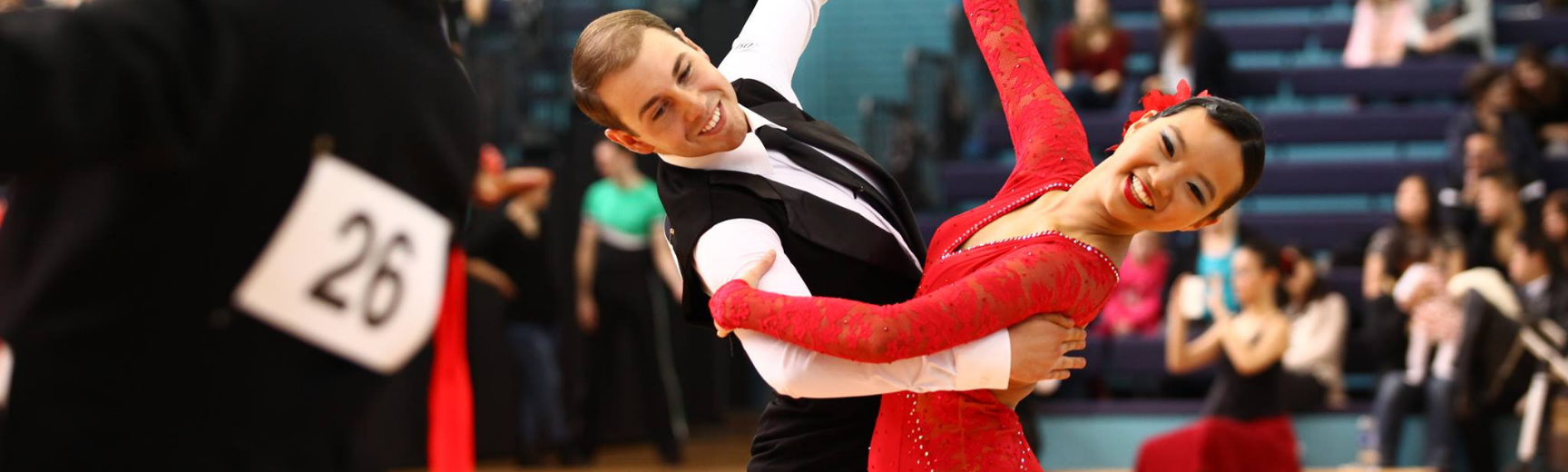 A man in a tuxedo dancing with a women in a red dress in a dancing competition