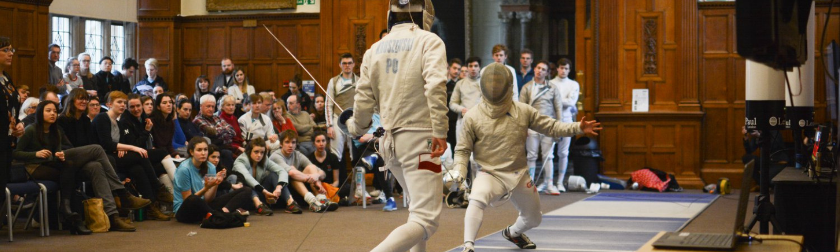 Two fencers competing with a large crowd watching on