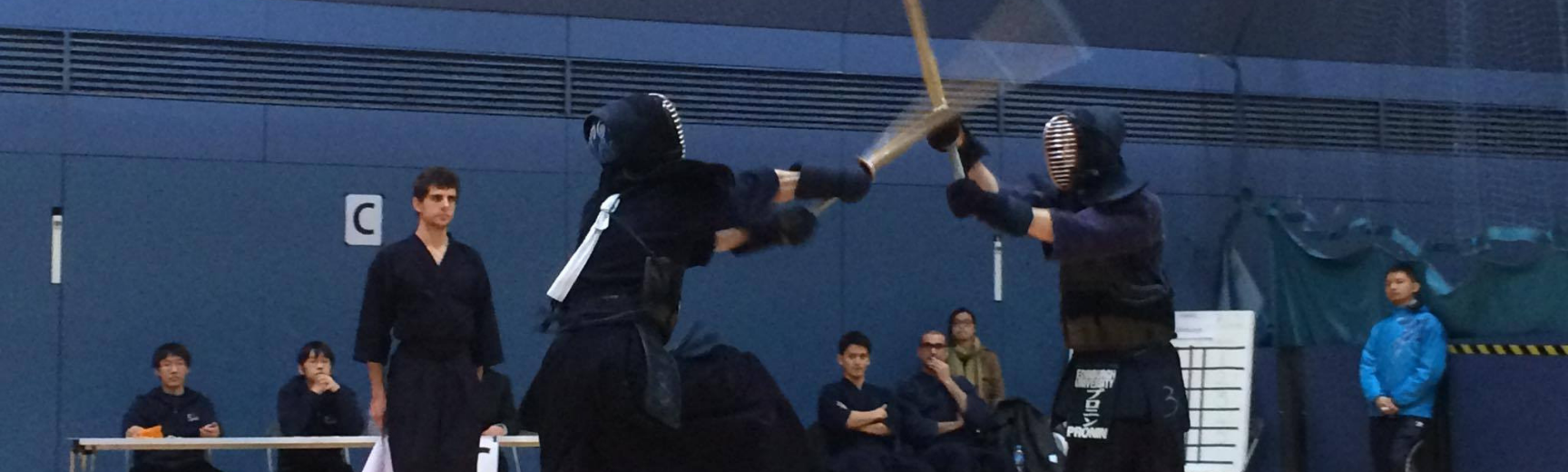 Two people in a kendo duel with a crowd watching behind them