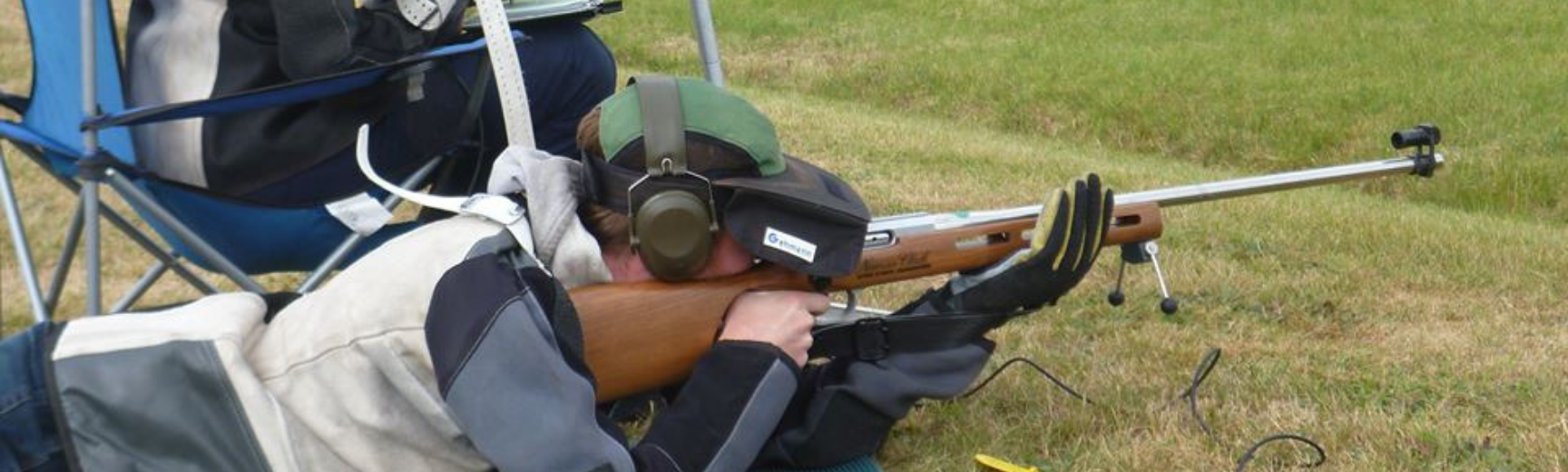 A man shooting a rifle from a prone position on the grass