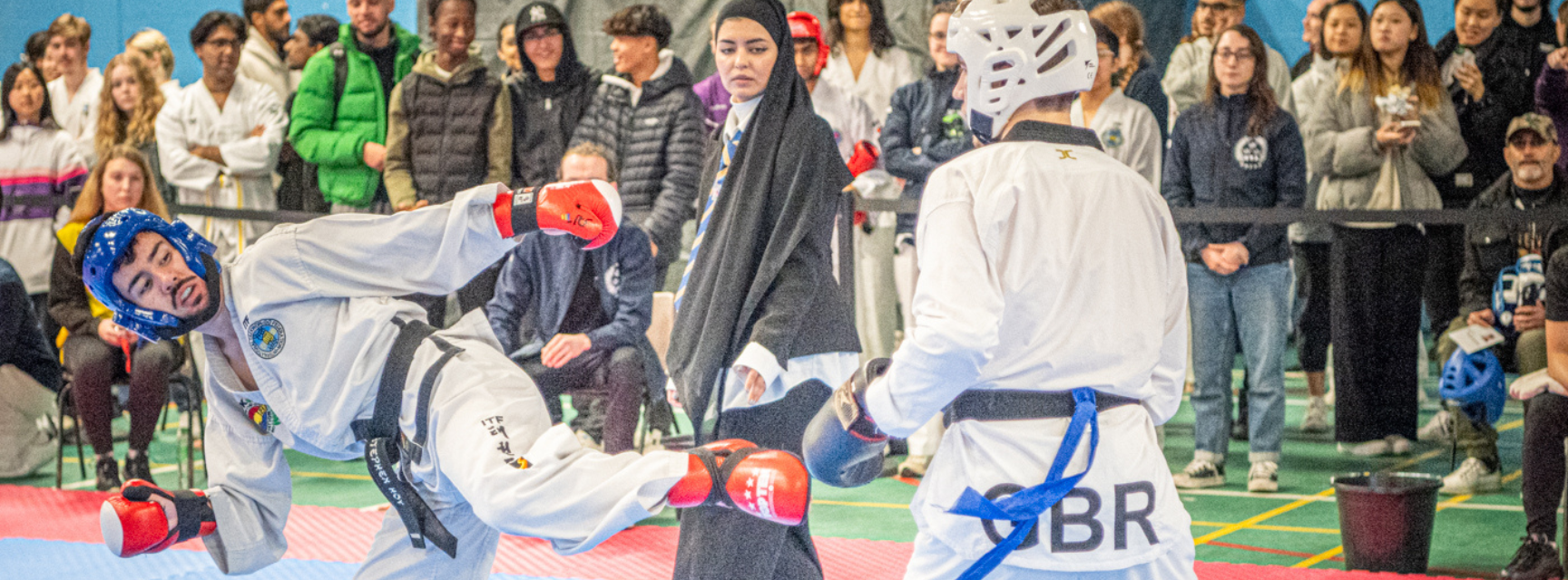 Two men competing in a taekwondo bout with a crowd watching on