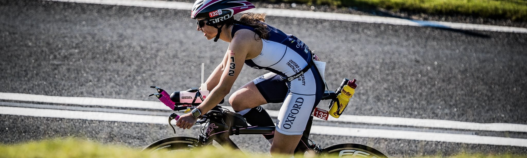 A triathlete riding her bike along a road, wearing Oxford dark blue kit