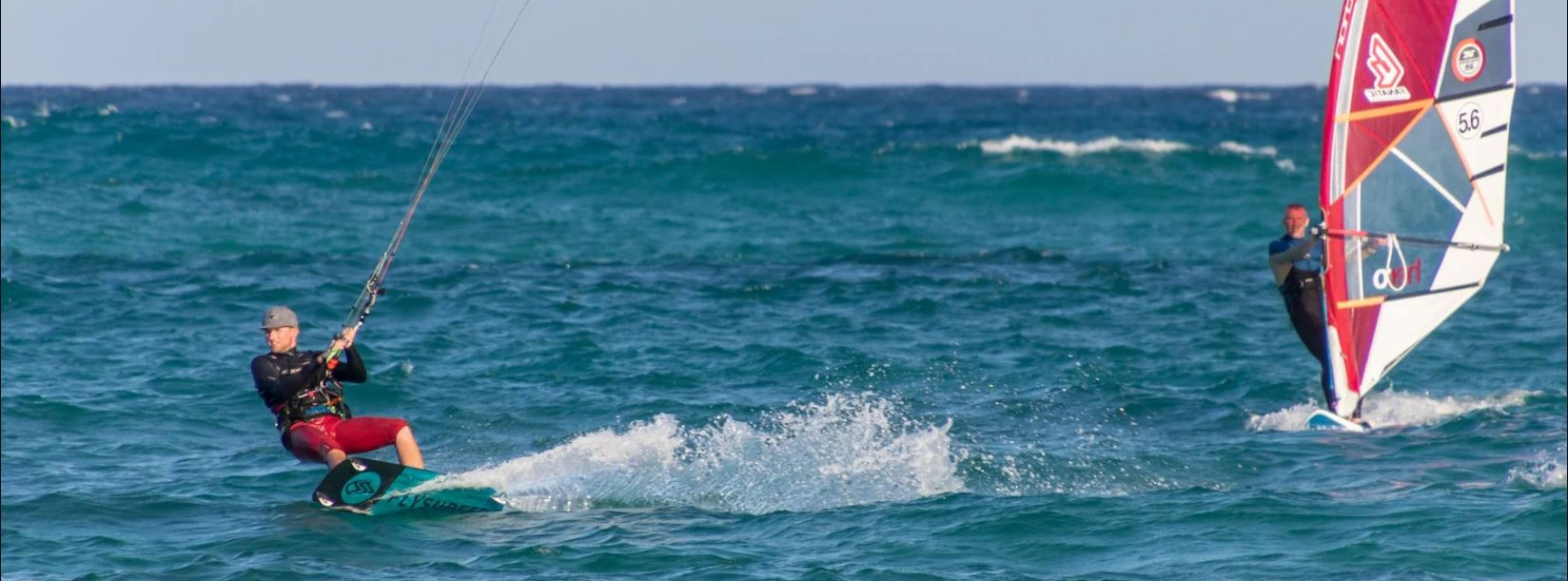 One windsurfer and one kitesurfer enjoying the waves in the sun