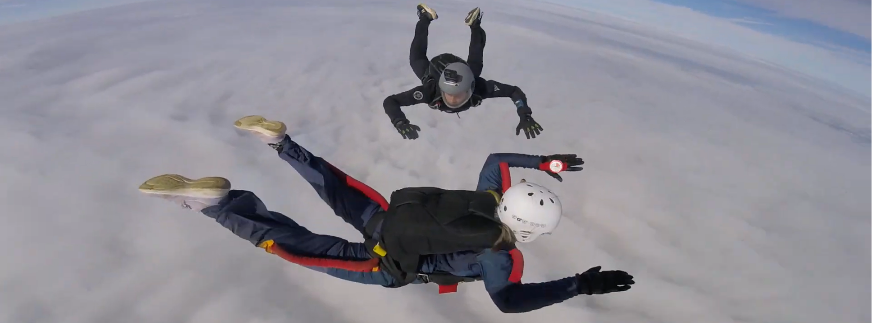 Two people skydiving with clouds visible underneath them