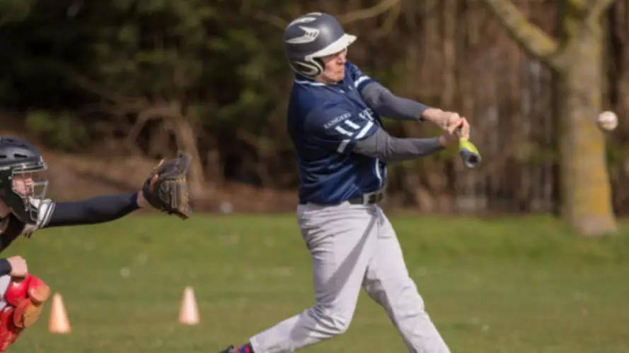 A man hitting a baseball shot, with a backstop behind waiting for him to miss