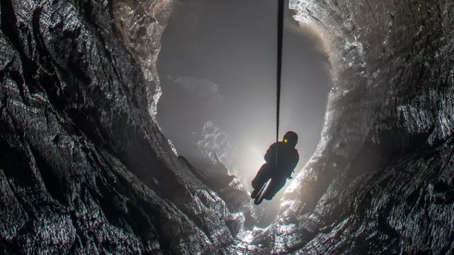 A caver being lowered down into a deep cave, with the cave lit from the bottom to create a dramatic image