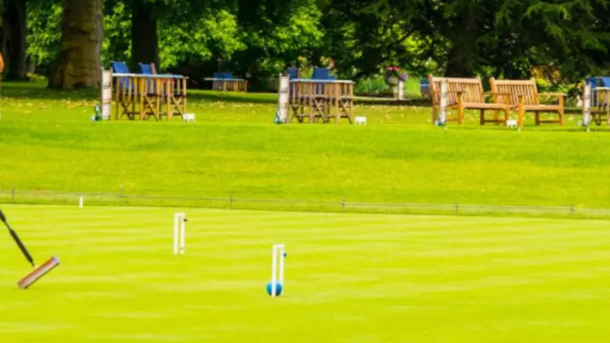 A man in all white hitting a croquet ball with a mallet, across a croquet lawn