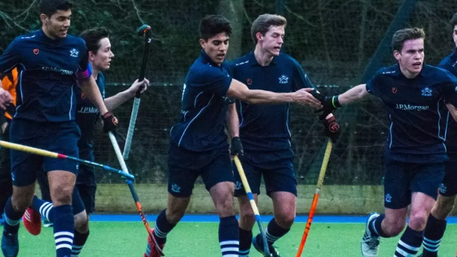 A men's hockey team in dark blue kits running towards the camera and celebrating