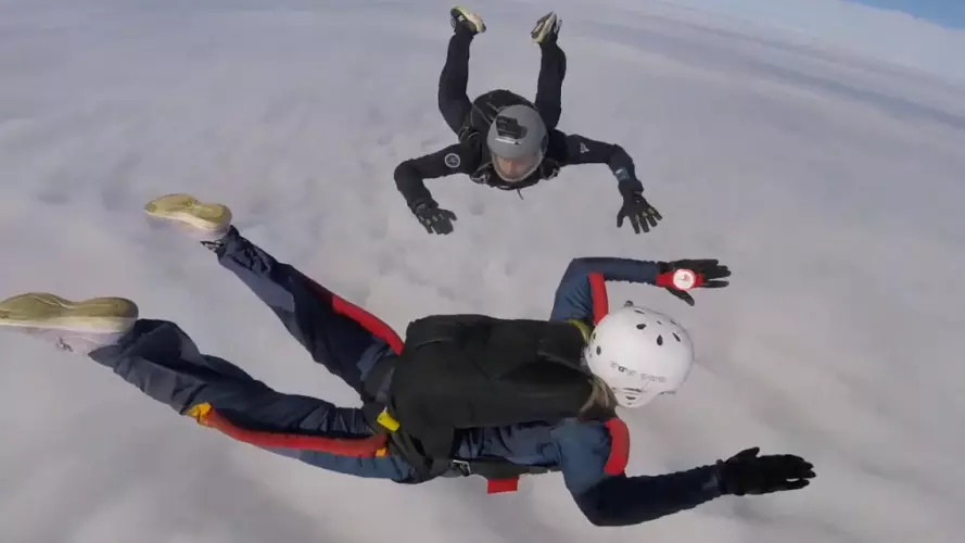 Two people skydiving with clouds visible underneath them