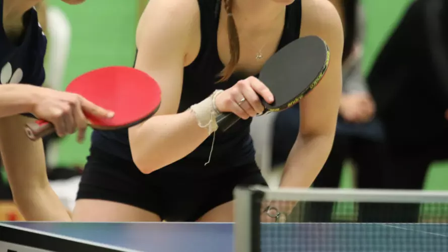 A close up of two women playing double table tennis