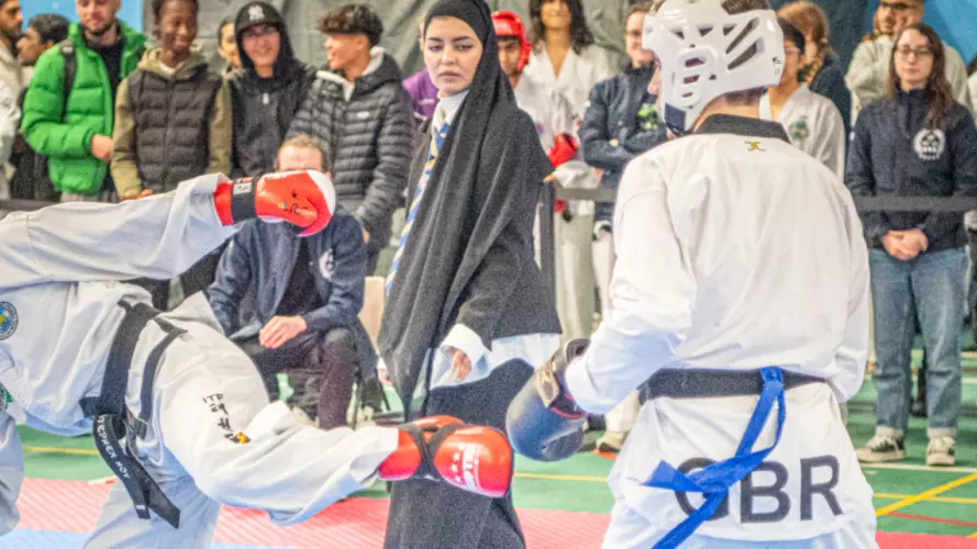 Two men competing in a taekwondo bout with a crowd watching on