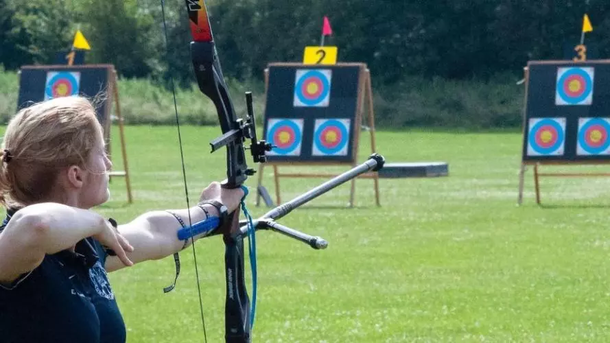 An archer with her bow pointed at a target, ready to shoot her next arrow